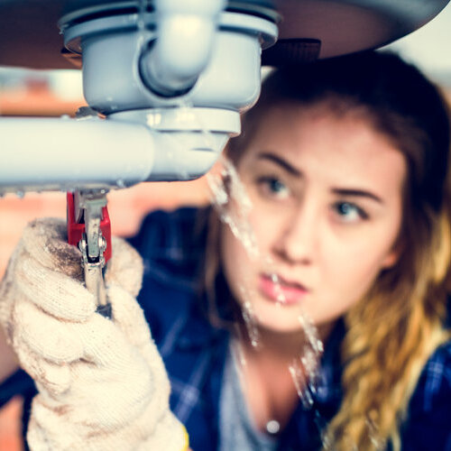 Woman using a wrench to fix a leaking pipe.